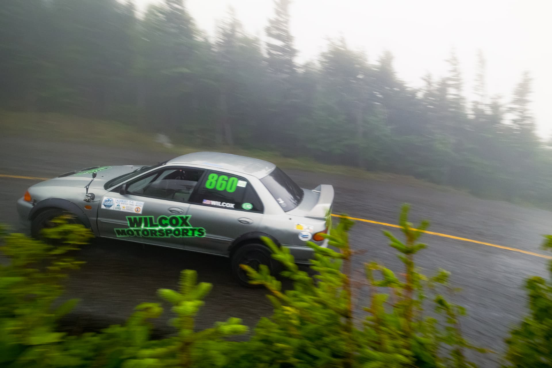 The grey Wilcox Motorsports Evolution #860 carving through mist and evergreen trees